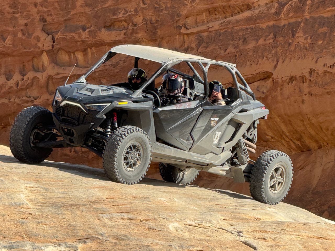 Piloto y copiloto en un UTV, el copiloto con el teléfono en la mano leyendo el mapa